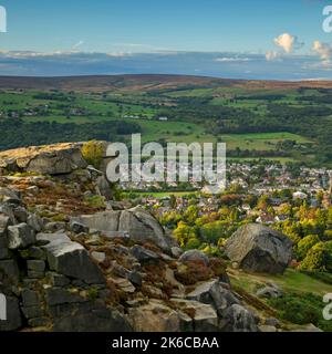 The Cow & Calf Rocks (scenic rural view overlooking village in Wharfe valley, high moorland crag, blue sky) - Ilkley Moor, West Yorkshire, England UK. Stock Photo
