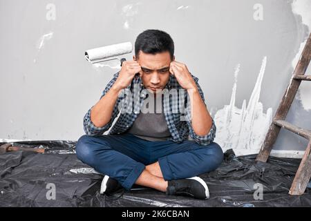 A young Asian man sits with head in hands overwhelmed by home DIY project Stock Photo