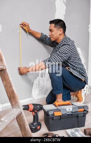 An Asian man measures against the wall using measuring tape doing home DIY Stock Photo