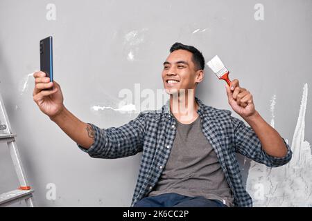 A young Asian man takes a selfie while busy with home improvement DIY project Stock Photo