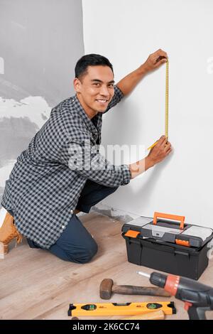 A young Asian man looks at the camera while measuring vertically for home DIY Stock Photo