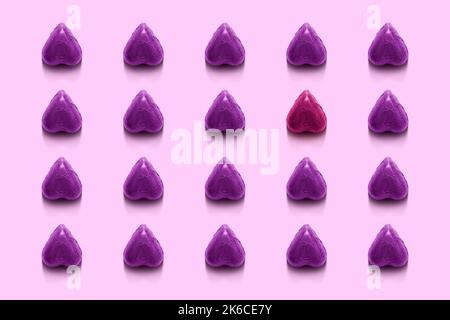 Pattern of heart shaped candies wrapped in foil with one red heart standing out from the line. Stock Photo