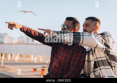Two cool Caucasian young men in checks shirts pointing fingers with blur beach background Stock Photo