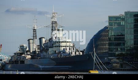 A telephoto view of HMS Belfast moored on River Thames with modern office buildings behind in London England. Stock Photo
