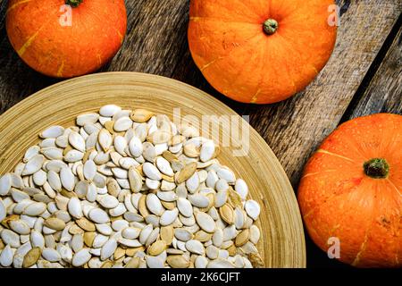 Pumpkins and pumpkin seeds in plate on wooden background Stock Photo