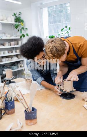 African american craftswoman helping man making clay cup in pottery studio,stock image Stock Photo