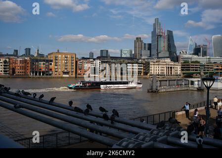 The Jupiter Clipper Thames clipper boat passes Millennium bridge travelling up river towards Bankside pier and past the financial district in the back. Stock Photo