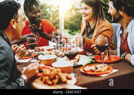 Happy family having barbecue party in backyard - Young friends celebrating at dinner drinking red wine at sunset - people food and drink lifestyle con Stock Photo