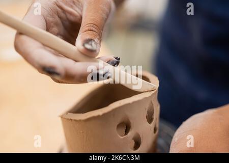Close up view of african american craftswoman using tool while making clay product in workshop,stock image Stock Photo