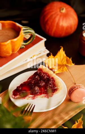 Cozy aesthetics home cherry pie, macaroons and cup of coffee in shape of pumpkin among candles and fragrant leaves. Hygge home aesthetic. Stock Photo