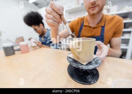 Blurred man painting on ceramic cup near african american girlfriend in pottery studio,stock image Stock Photo