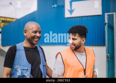 Happy young construction worker talking with bald colleague at site Stock Photo