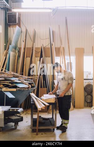 Full length of male carpenter reading blueprint at workbench in workshop Stock Photo