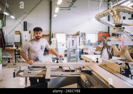 Portrait of young carpenter standing by machinery in workshop Stock Photo