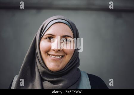 Portrait of smiling female construction worker wearing headscarf against wall Stock Photo
