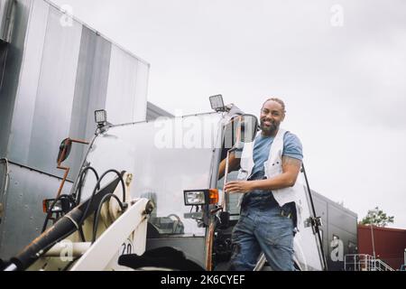 Low angle view of male construction standing at doorway of vehicle Stock Photo