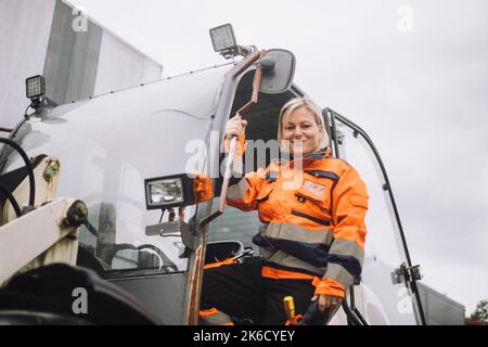 Portrait of smiling female construction worker standing at doorway of vehicle Stock Photo