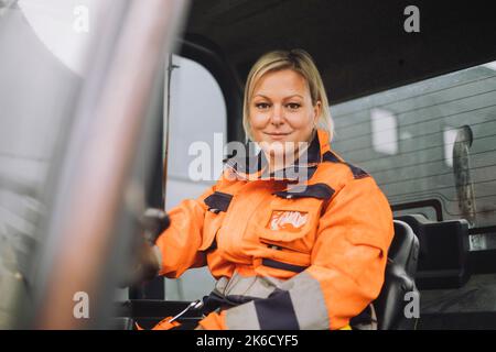 Smiling female construction worker in reflective clothing sitting in vehicle Stock Photo