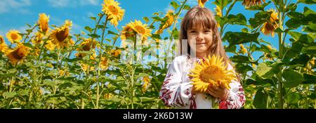 A child in a field of sunflowers in an embroidered shirt. Ukrainian. Selective focus. Stock Photo