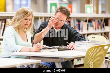 Adult Education: Library Revision. A pair of mature students working together in a college project. From a series of related images on the subject. Stock Photo