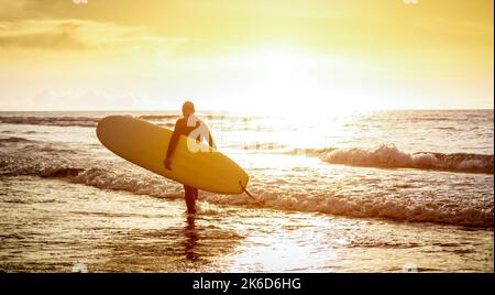 Guy surfer walking with surfboard at sunset in Tenerife - Surf long board training practitioner in action - Sport travel concept with sof focus water Stock Photo