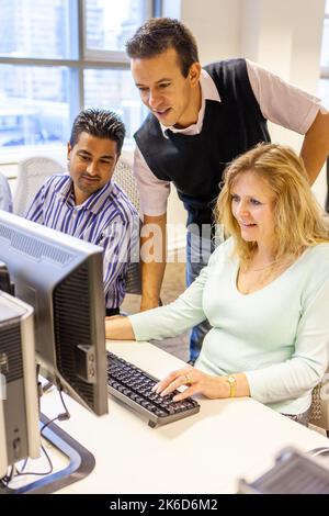 Adult Education: Working Together. A teacher helping mature students in their college computer suite. From a series of related images on the subject. Stock Photo