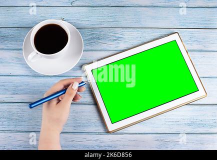 Male hands holding tablet pc with green empty screen on wooden background. Stock Photo