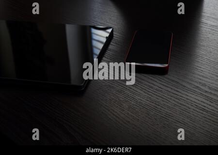 Tablet and mobile phone lying on the wooden table in the dark Stock Photo