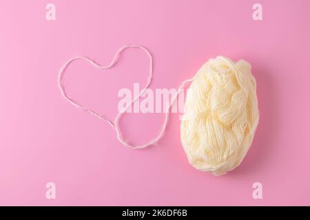 Top view of heart made from a woolen thread with ball of yarn on light pink background Stock Photo