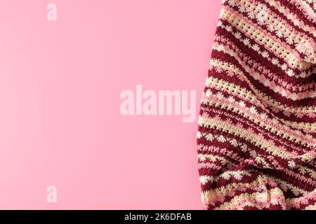Top view of colorful handmade crochet blanket on pastel pink background with copy space, mockup Stock Photo