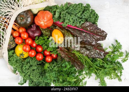 Eco shopping concept, colorful vegetables broccoli cauliflower carrots tomatoes kale pak choy onions chard in net bag. Healthy local farm produce on white wooden table, top view, selective focus Stock Photo