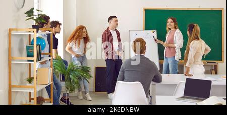 Team of college students presents their project together in classroom near whiteboard. Stock Photo