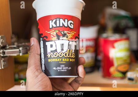 Adult male picking an Pot noodles from home food cupboard Stock Photo