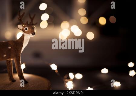 Miniature reindeer on wooden tray, with glowing string lights in the background. Christmas wallpaper with copy space. Stock Photo