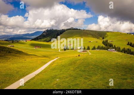 A narrow trail on lush green hill with scattered houses in the background Stock Photo