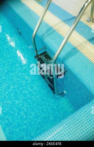 Pool ladder with stairs in empty pool for sport swimming training in leisure center.Ladder stainless handrails for descent into swimming pool Stock Photo