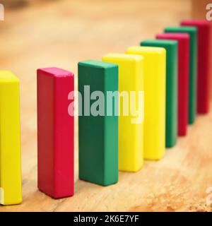 Wooden building blocks for a preschool classroom or child are standing up right in red, yellow and green to form a row and fall down like dominoes Stock Photo