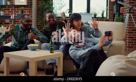Cheerful people having fun with photos on smartphone, taking pictures and fooling around. Laughing at images on mobile phone, making funny memories and enjoying leisure activity. Stock Photo
