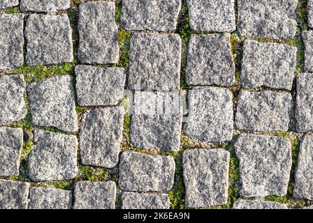 Stone road paved with asymmetrical stones with sprouted grass at seams. Textured background, top view Stock Photo