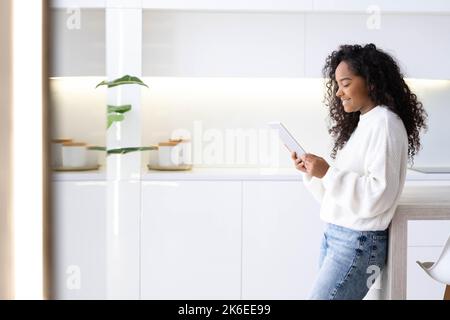 African American Girl using digital tablet at home pressing finger, reading social media internet, typing text or shopping online. Freelancer Remotely Stock Photo