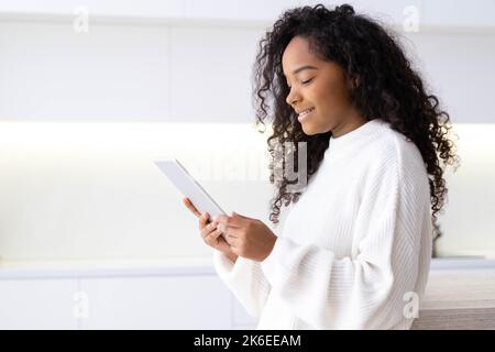 African American Girl using digital tablet at home pressing finger, reading social media internet, typing text or shopping online. Freelancer Remotely Stock Photo