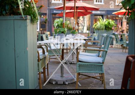 empty folding tables and large umbrella / Parasol at cafe with plants, glass cups and wicker chairs Stock Photo