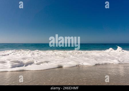Low angle view of ocean wave washing up onto sandy beach under a blue sky Stock Photo