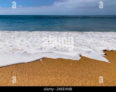 Low angle view of ocean wave washing up onto sandy beach under a blue sky Stock Photo