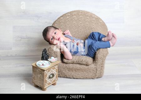 new born baby boy in beautiful dress lying at little chair,tiny stool small toys,face expressions,arabic infant kid,soft skin Stock Photo