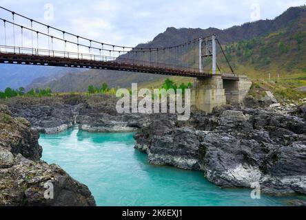 Orokto bridge on the Katuni River. A suspension bridge on the rocky banks of a mountain river with emerald water. Altai Republic, Siberia, Russia, 202 Stock Photo