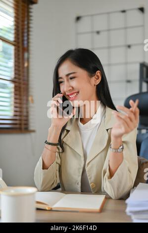 Portrait, Attractive and confident young Asian businesswoman or female account executive in the office, talking on the phone with her business client. Stock Photo