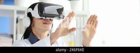 Young female doctor in virtual reality headset works on computer in hospital office Stock Photo