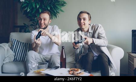 Careless students playing video game watching screen and pressing joystick buttons. Friendship and technology concept. Stock Photo
