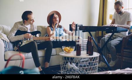Young friends musicians are practising at home singing and playing guitar and keyboard. Musical instruments, attractive creative people, friendship and hobby concept. Stock Photo